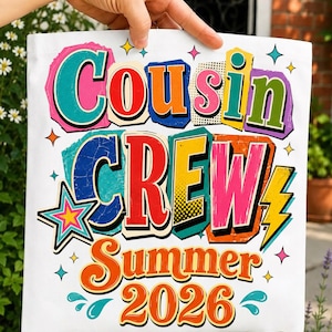 May include: A white tote bag featuring a colorful graphic with the text "Cousin CREW Summer 2026". The design includes bold, multi-colored letters with distressed textures, a star, a lightning bolt, and small decorative shapes in shades of pink, blue, orange, and yellow.