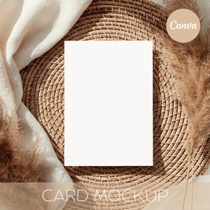 May include: A blank white card mockup on a woven wicker placemat, with a beige fabric and dried ornamental grass. The card is centered, with the text "CARD MOCKUP" at the bottom. A circular "Canva" logo is in the upper right corner.