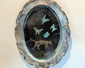 May include: An oval, silver-toned tray with a beaded turquoise border. The tray's center features a black background with a cat silhouette and green butterfly designs. The tray has ornate, decorative edges.