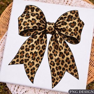 May include: A decorative bow featuring a tan and brown leopard print pattern with black outlines. The bow has two large loops at the top and two long, pointed tails extending downwards, creating a symmetrical shape on a white background.