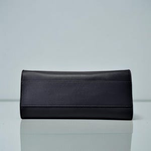 May include: A black leather clutch wallet with a rectangular shape. The wallet has a smooth texture with a horizontal seam detail across the center. The design is simple and elegant, suitable for various occasions.