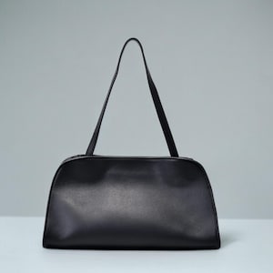 May include: A black handbag with a rectangular body and a curved top. The bag has two thin, long straps and a zipper closure. The bag is made of a smooth, shiny material.