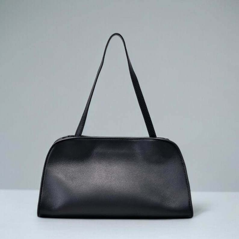 May include: A black handbag with a rectangular body and a curved top. The bag has two thin, long straps and a zipper closure. The bag is made of a smooth, shiny material.