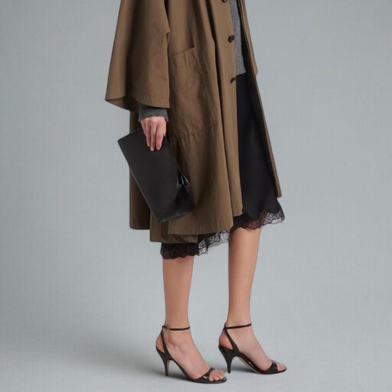 May include: A person wearing a brown coat, gray sweater, and black skirt with lace trim. They are holding a black clutch and wearing black heeled sandals.