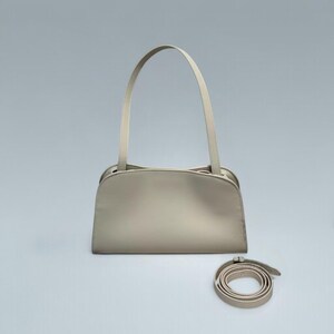 May include: A light beige handbag with a curved top and long, thin handles. A matching, detachable shoulder strap is coiled at the bottom. The bag has a minimalist design and a smooth texture, suitable for everyday use.