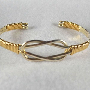May include: A gold and silver wire wrapped bracelet with a knot design.