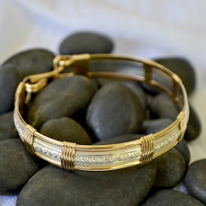 May include: A gold and silver wire wrapped bracelet with a delicate pattern. The bracelet is made of two different metals, creating a unique and stylish look.