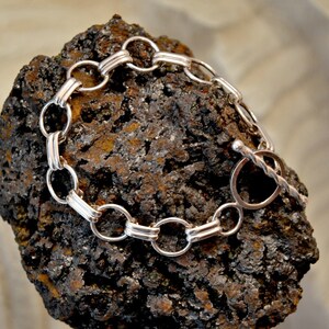 May include: A silver chain bracelet with a toggle clasp. The chain is made of interlocking oval links with a decorative detail on each link.