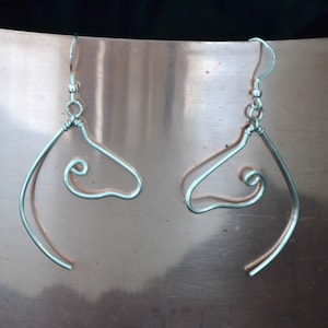 May include: A pair of silver wire earrings shaped like a stylized human profile. The earrings are made of thin wire and have a simple, minimalist design.