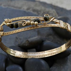 May include: A gold wire-wrapped bracelet with brown and black stones and gold beads.