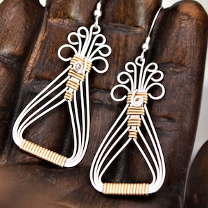 Peut inclure: Une paire de boucles d'oreilles en fil d'argent et d'or avec un design délicat et complexe. Les boucles d'oreilles sont en forme de larme avec un petit groupe décoratif de fil en haut.
