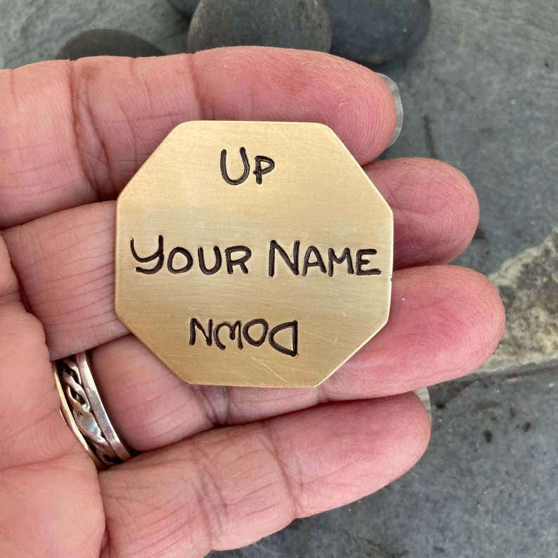 May include: A gold-colored octagonal metal tag with the words "Up", "Your Name", and "Down" engraved on it.