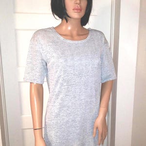 May include: A short-sleeved t-shirt in a light gray heathered fabric with a round neckline. The garment features a textured, speckled appearance throughout the material, providing a consistent gray tone across the front of the shirt.