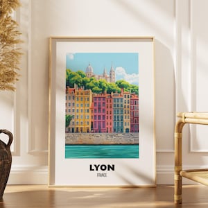 May include: A framed vertical art print featuring a colourful illustration of Lyon, France, with a row of multi-coloured buildings along a riverbank, a green hillside, and a domed building at the top. The text LYON FRANCE is printed at the bottom.