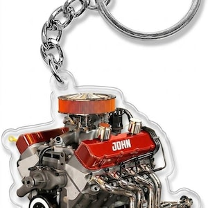 May include: Keychain featuring a detailed illustration of a red and silver engine. The engine has a chrome exhaust system and an orange air filter. The word "JOHN" is printed on the engine. The keychain includes a chain and a silver key ring.