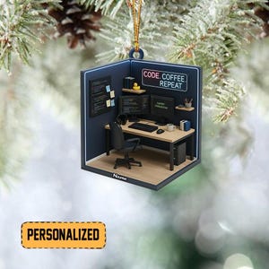 Pode incluir: Um enfeite decorativo em forma de espa&ccedil;o de trabalho de um programador. O enfeite apresenta uma mesa com dois monitores, um teclado e uma caneca de caf&eacute;. O texto "CODE. COFFEE. REPEAT" &eacute; exibido. O enfeite &eacute; personalizado com a palavra "Name" e a palavra "PERSONALIZED".