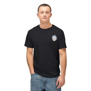 May include: Black t-shirt featuring a small, embroidered cartoon character design on the upper left chest. The design is a light blue and gray face with a light blue starburst. The person is wearing blue jeans.