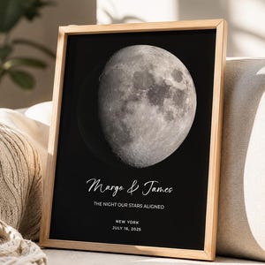 Könnte beinhalten: Ein gerahmter Druck mit einem detaillierten, kontrastreichen Bild des Mondes vor schwarzem Hintergrund. Der Text lautet Margo & James, THE NIGHT OUR STARS ALIGNED, NEW YORK und JULY 16, 2025. Der Rahmen besteht aus hellem Holz.