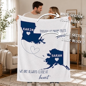 May include: A white fleece blanket featuring two dark blue state silhouettes, Louisiana and Alaska, connected by a dashed line forming a heart. The text reads: KARIN, SARAH, THOUGH WE MAYBE MILES apart, and WE ARE ALWAYS CLOSE AT heart.