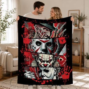 May include: A black fleece blanket featuring a graphic print of four horror movie characters arranged in horizontal panels. The design includes Freddy Krueger, Jason Voorhees, Pennywise, and Michael Myers, accented with red blood splatter and handprints.