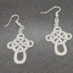 May include: A pair of silver-colored Celtic knot earrings. Each earring features a looped design with a cross-like knot at the top and a teardrop shape at the bottom. The earrings hang from a simple hook.