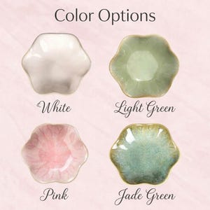 K&ouml;nnte beinhalten: Vier blumenf&ouml;rmige Keramikschalen in einem Raster angeordnet. Oben links wei&szlig;, oben rechts hellgr&uuml;n, unten links rosa, unten rechts jadegr&uuml;n. Der Text Color Options erscheint dar&uuml;ber, mit den Beschriftungen White, Light Green, Pink, Jade Green.