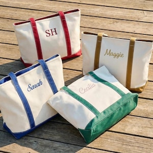 Puede incluir: Cuatro bolsas de lona con diferentes acentos de color y nombres o iniciales bordados. Las bolsas tienen acentos rojos, azules, verdes y dorados. Los nombres "SH", "Sarah", "Maggie" y "Cecilia" están bordados en las bolsas.