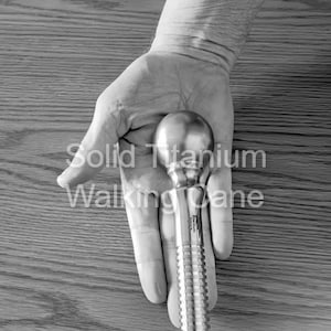 May include: A solid titanium walking cane with a rounded handle and a textured shaft. The text "Solid Titanium Walking Cane" is printed on the image.