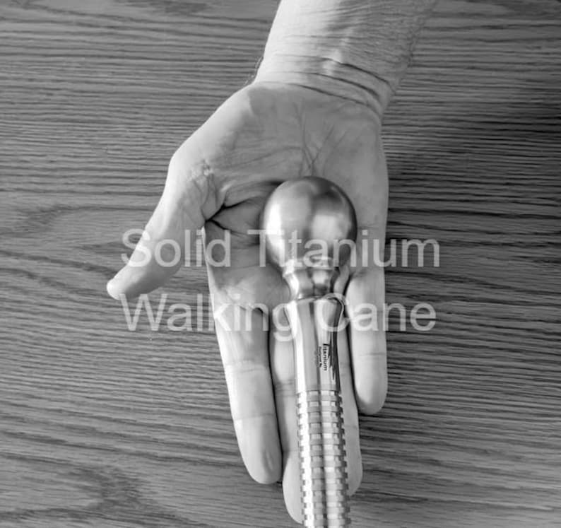 May include: A solid titanium walking cane with a rounded handle and a textured shaft. The text "Solid Titanium Walking Cane" is printed on the image.