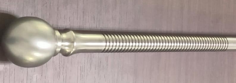 May include: A silver-colored curtain rod with a spherical finial. The rod has a spiral design along its length. The rod is made of metal and is designed to hang curtains.
