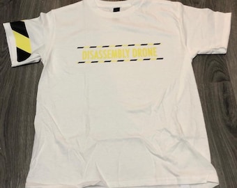 May include: White t-shirt with the text "DISASSEMBLY DRONE" in yellow and black. The left sleeve has a black and yellow graphic. The shirt is made of a soft material.