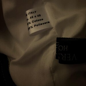 May include: Close-up of a white fabric tag with text. The tag reads "MADE IN ITALY", followed by measurements "cm. 45 x 45", and fabric composition details: "100% Cotone" and "100% Poliestere".