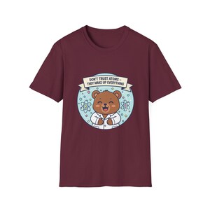 Peut inclure: T-shirt bordeaux avec un ours de dessin animé en blouse de laboratoire, entouré d'illustrations d'atomes. L'ours sourit, et une bannière indique : « DON'T TRUST ATOMS - THEY MAKE UP EVERYTHING ».