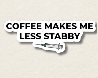 May include: A white sticker with black text that reads "COFFEE MAKES ME LESS STABBY." A small illustration of a syringe is below the text. The sticker has a white border and is on a textured, off-white background.