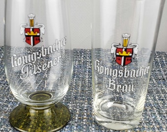 Könnte beinhalten: Zwei klare Biergläser. Eines hat einen grün getönten Boden und den Text "Konigsbacher Pilsener". Das andere Glas hat den Text "Konigsbacher Brau" und ein rot-goldenes Wappen.