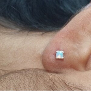 May include: A close-up of a person's ear with a small, white opal stud earring.