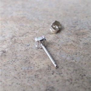 May include: A silver earring with a small, iridescent opal gemstone. The earring has a post and a butterfly back.