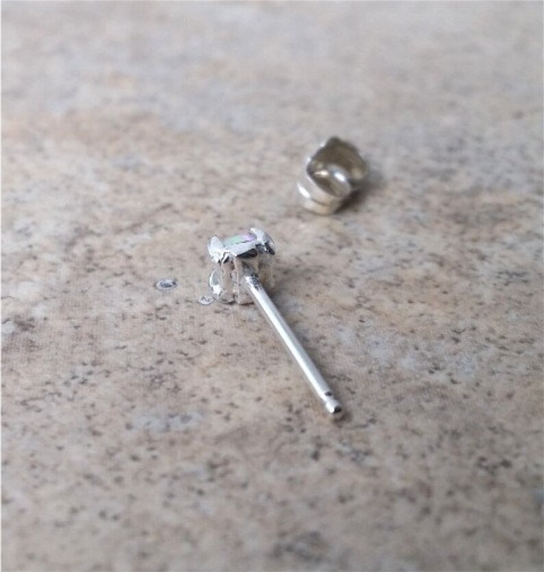 May include: A silver earring with a small, iridescent opal gemstone. The earring has a post and a butterfly back.