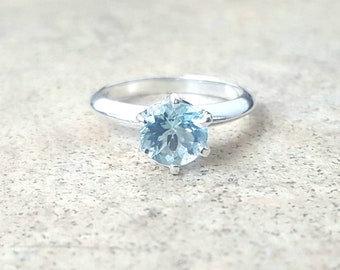Pode incluir: Um anel de prata com uma gema azul claro engastada em garras.