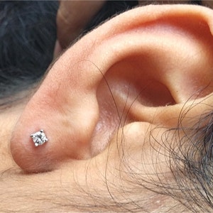 May include: A close-up of a person's ear with a small, clear diamond stud earring.
