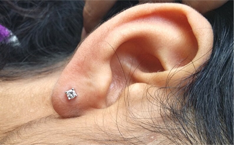 May include: A close-up of a person's ear with a small, clear diamond stud earring.