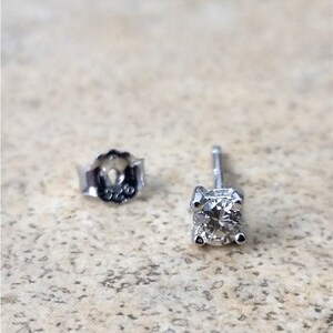 May include: A pair of silver stud earrings with a small, clear diamond in each earring. The back of the earring is marked with "925".