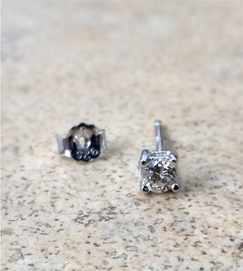 May include: A pair of silver stud earrings with a small, clear diamond in each earring. The back of the earring is marked with "925".