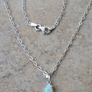 May include: A silver chain necklace with a teardrop-shaped opal pendant.