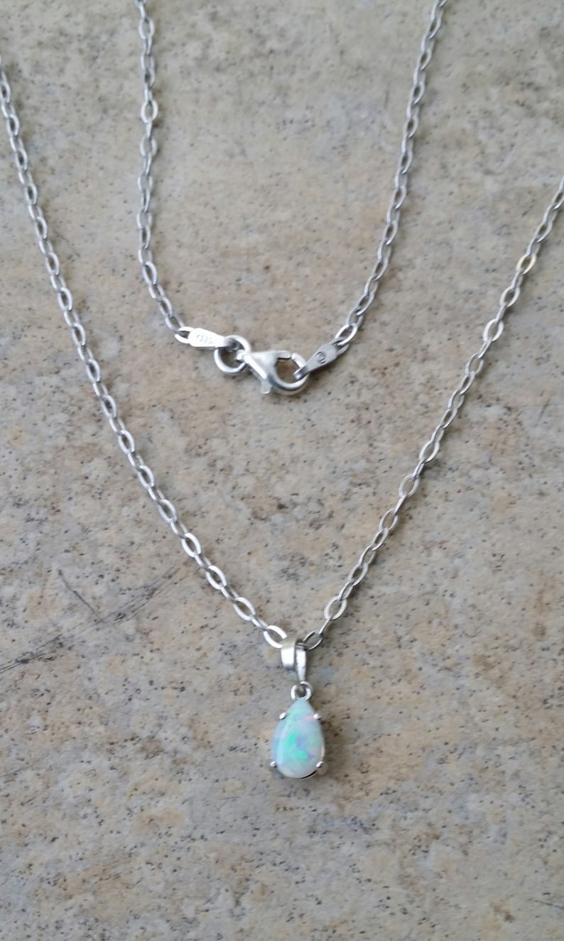 May include: A silver chain necklace with a teardrop-shaped opal pendant.