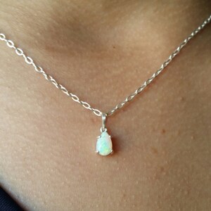 May include: A silver chain necklace with a teardrop-shaped opal pendant.