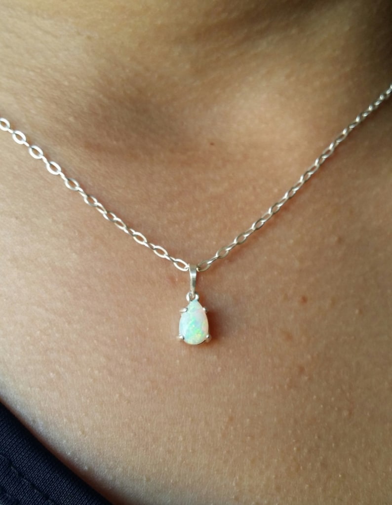 May include: A silver chain necklace with a teardrop-shaped opal pendant.