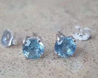 May include: A pair of silver stud earrings with round, light blue gemstones.