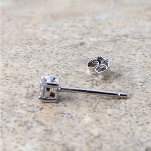 May include: A silver stud earring with a small, clear gemstone. The earring has a post and a butterfly back.