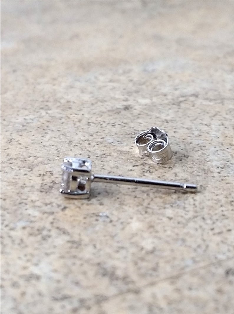 May include: A silver stud earring with a small, clear gemstone. The earring has a post and a butterfly back.